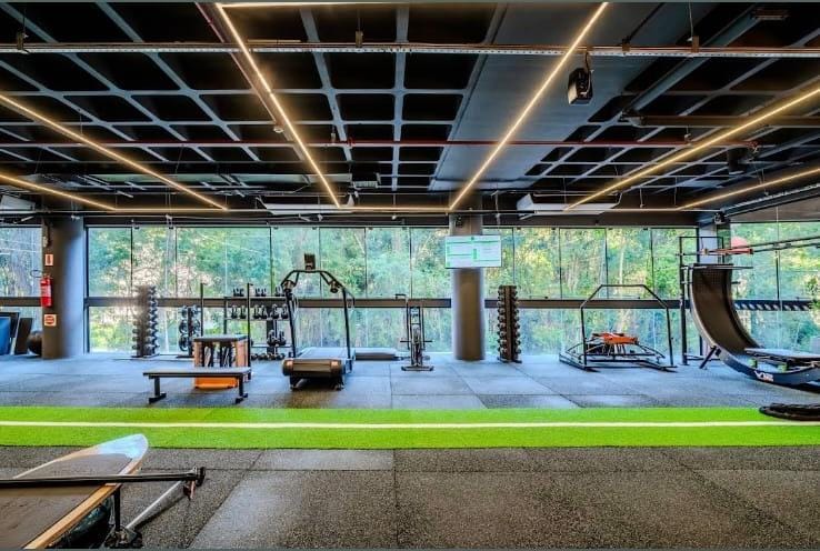 Salão de treino do Studio Integrado Mormaii Fitness, com janelas de vidro voltadas para a mata